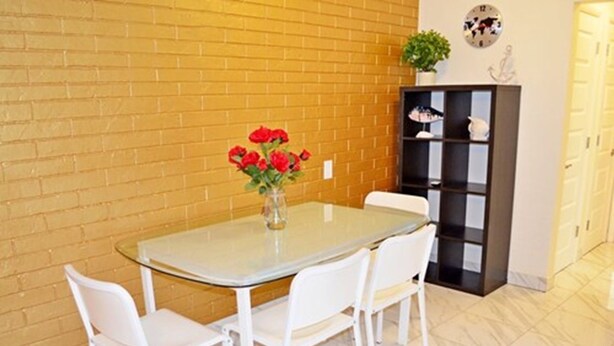 A dining area with a glass table, white chairs, and a vase of red flowers.