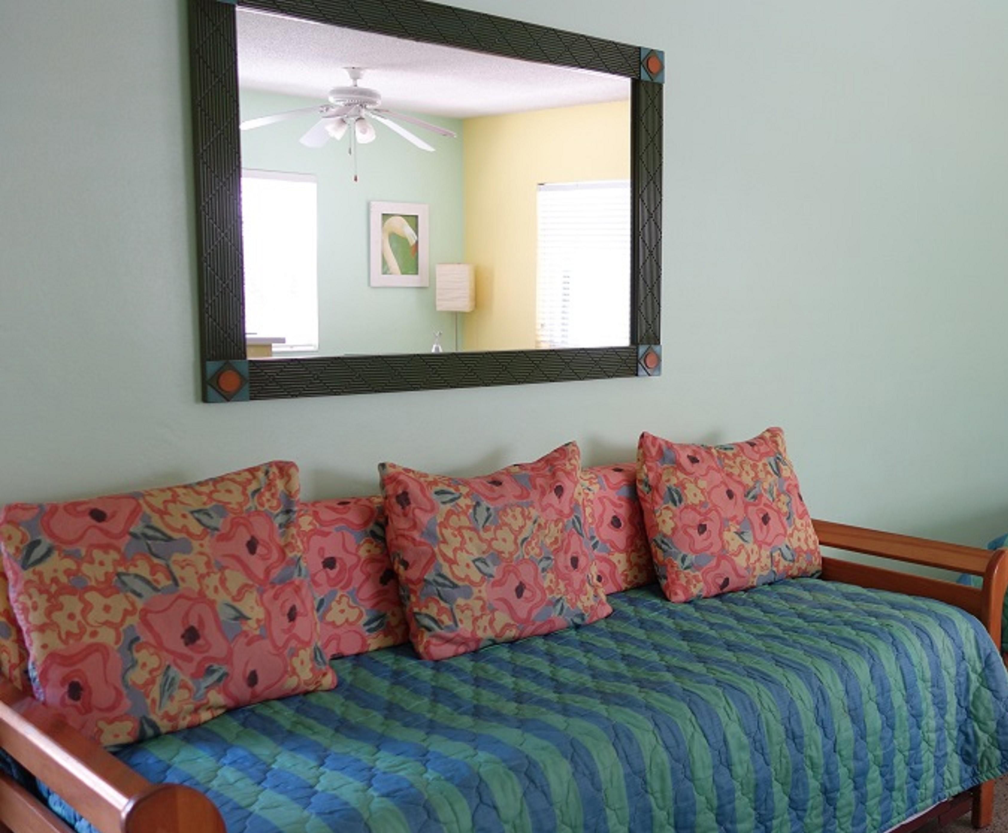 A bedroom with a bed, floral-patterned pillows, a green quilt, and a large mirror on the wall.