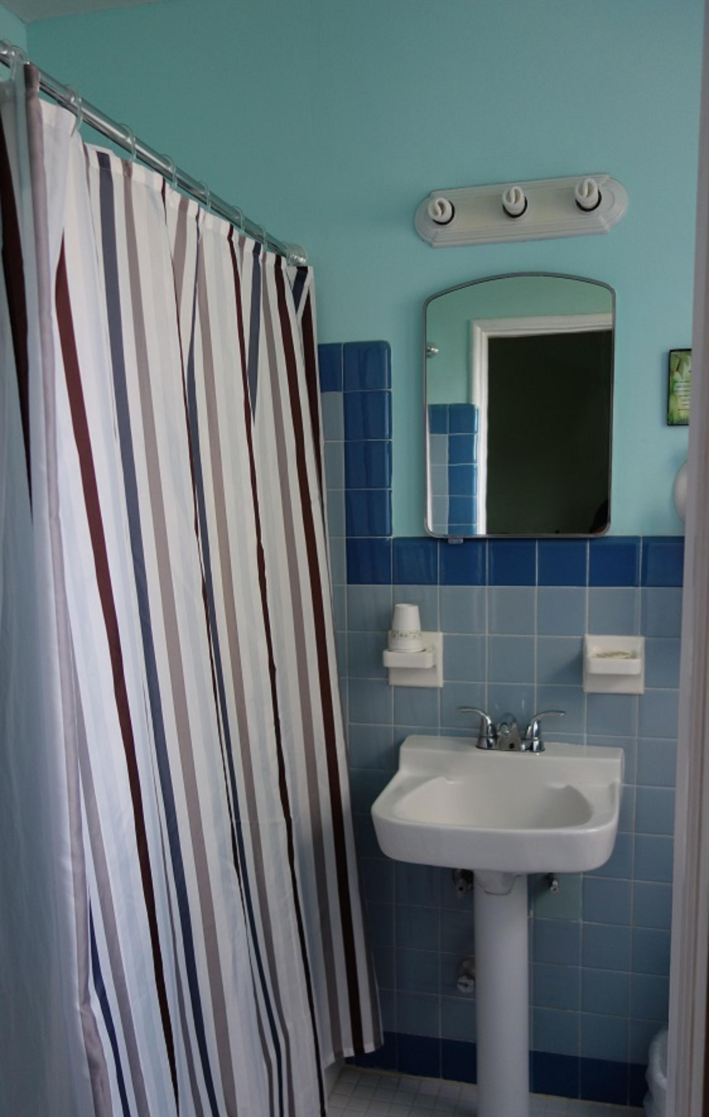 A bathroom with a striped shower curtain, a sink, a mirror, and blue-tiled walls.