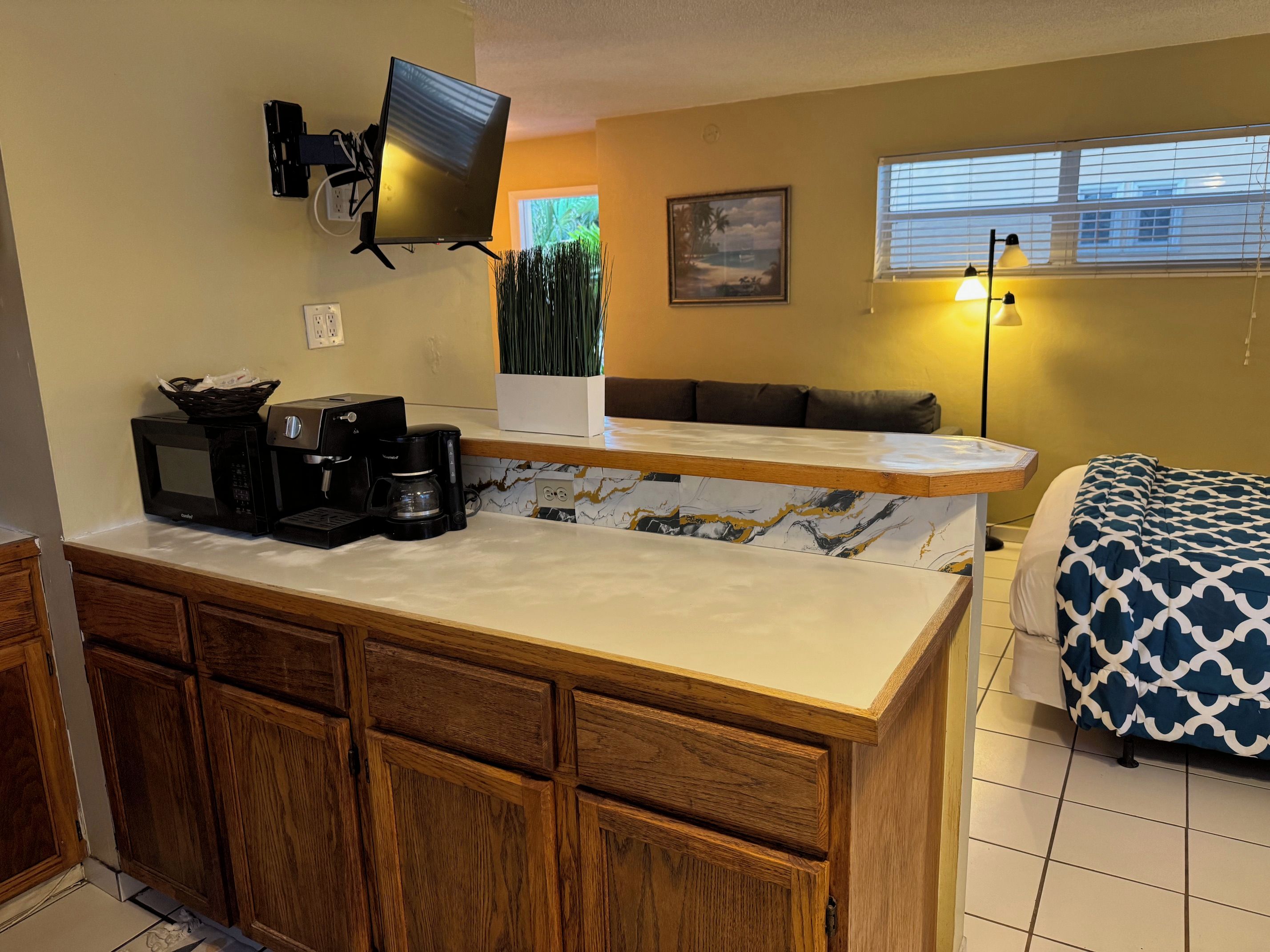 A compact kitchen with a microwave, coffee maker, and a flat-screen TV mounted on the wall.