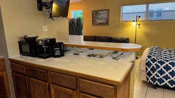 A compact kitchen with a microwave, coffee maker, and a flat-screen TV mounted on the wall.
