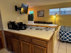 A compact kitchen with a microwave, coffee maker, and a flat-screen TV mounted on the wall. - Ocean Inn (Hollywood)