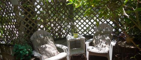 Deux fauteuils Adirondack, séparés par une petite table, sont placés devant une clôture en treillis de bois ornée de verdure.