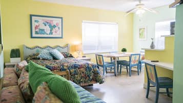 Um quarto aconchegante com cama, sofá, mesa de jantar com cadeiras e um ventilador de teto.