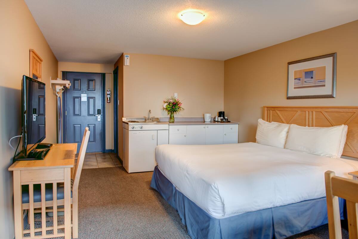 Habitación de hotel con cama, escritorio, silla, kitchenette y baño.