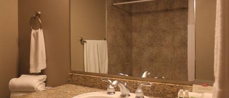 A bathroom with a granite countertop sink, two faucets, a mirror, and a towel rack with folded towels.