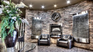 A modern living room with stone walls, a fireplace, leather sofas, and a large potted plant. - Podollan Inn & Spa Grande Prairie (Grande Prairie)