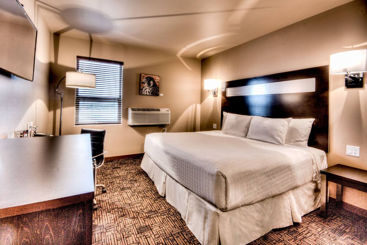 Una camera d'albergo con un letto, una scrivania, una lampada, un condizionatore d'aria a parete e un quadro.