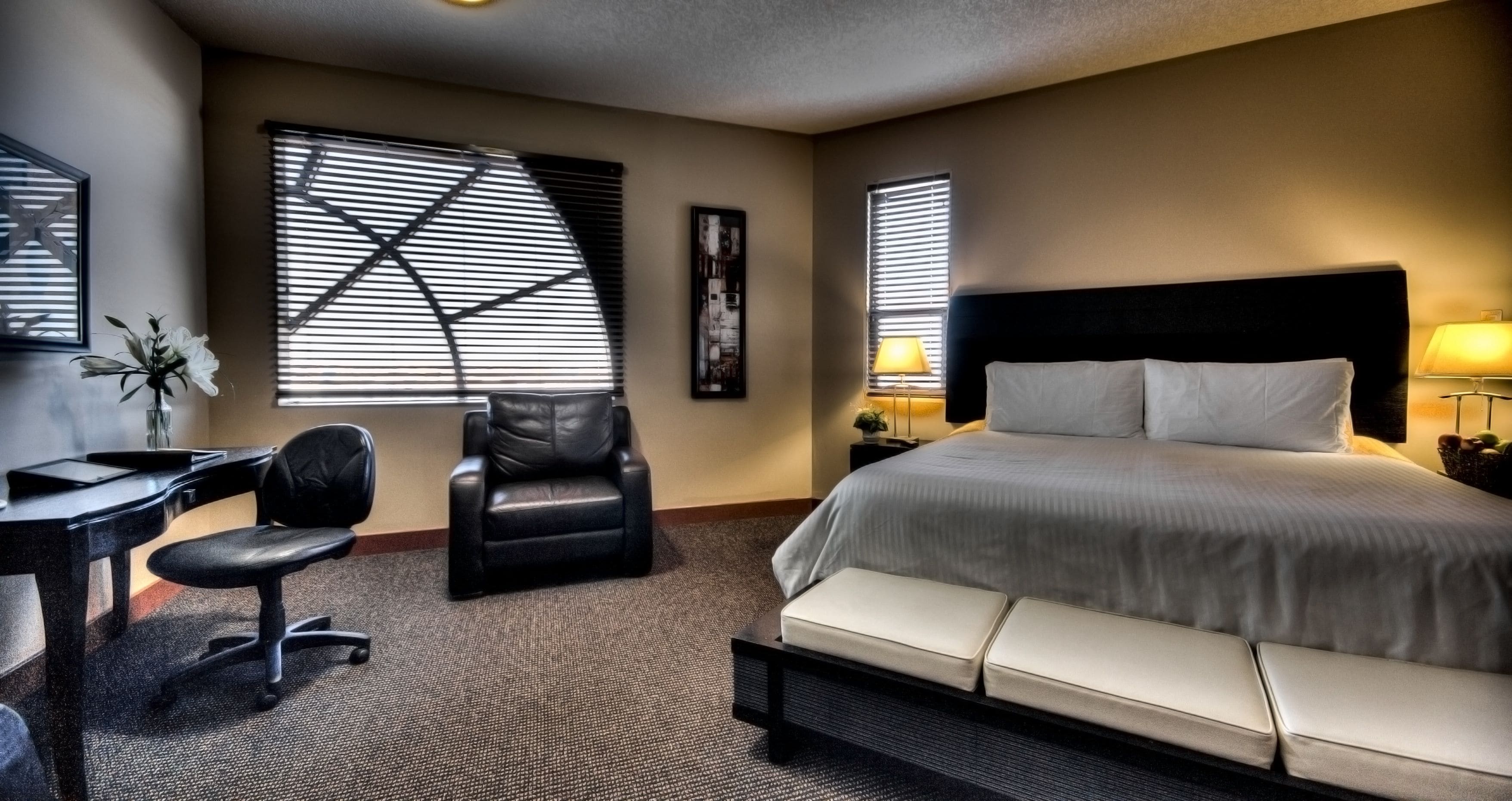 A hotel room with a bed, a desk, a chair, and a window with blinds.