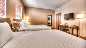 A hotel room with two beds, a desk, a chair, a lamp, a TV, and a mirror.