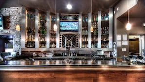 A bar area with a stone wall, shelves of liquor bottles, a TV screen, and a bar counter with a wine cooler. - Podollan Inn & Spa Grande Prairie (Grande Prairie)
