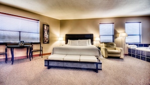 A hotel room with a large bed, a desk, two chairs, and a bathroom with a bathtub. - Podollan Inn & Spa Grande Prairie (Grande Prairie)