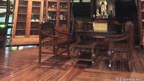 Quarto com teto alto, vigas de madeira, um candelabro, área de bar com garrafas e um armário com copos.