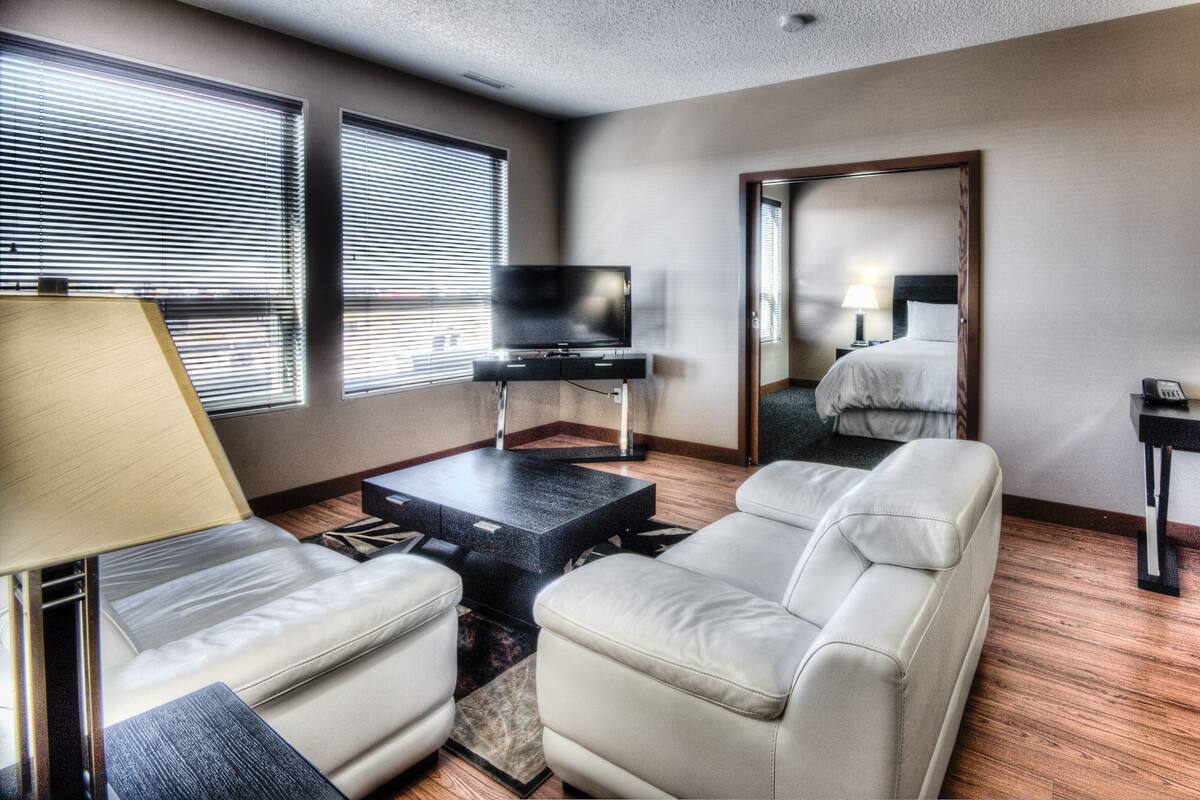 A hotel room with a sofa, a TV on a stand, a desk with a chair, and a mirror.