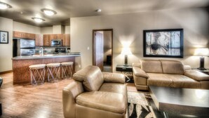 A modern living room with a leather sofa, a coffee table, and a kitchen area with a bar stool. - Grand Inn & Residence (Grande Prairie)
