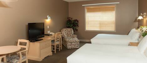 A hotel room with a bed, a desk with a television, a chair, a small table, and a window with blinds.