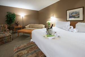 Habitación de hotel con una cama grande, un sofá, una mesita de centro, una planta en maceta y un cuadro en la pared.