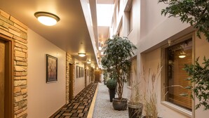 Un couloir d’hôtel avec un sol à motifs, des plantes en pot et un luminaire au plafond.