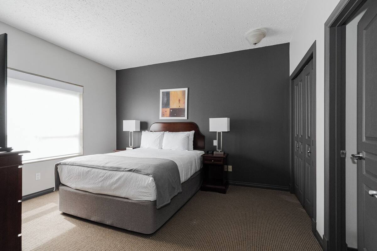 A hotel room with a large bed, bedside lamps, a window, and a door.