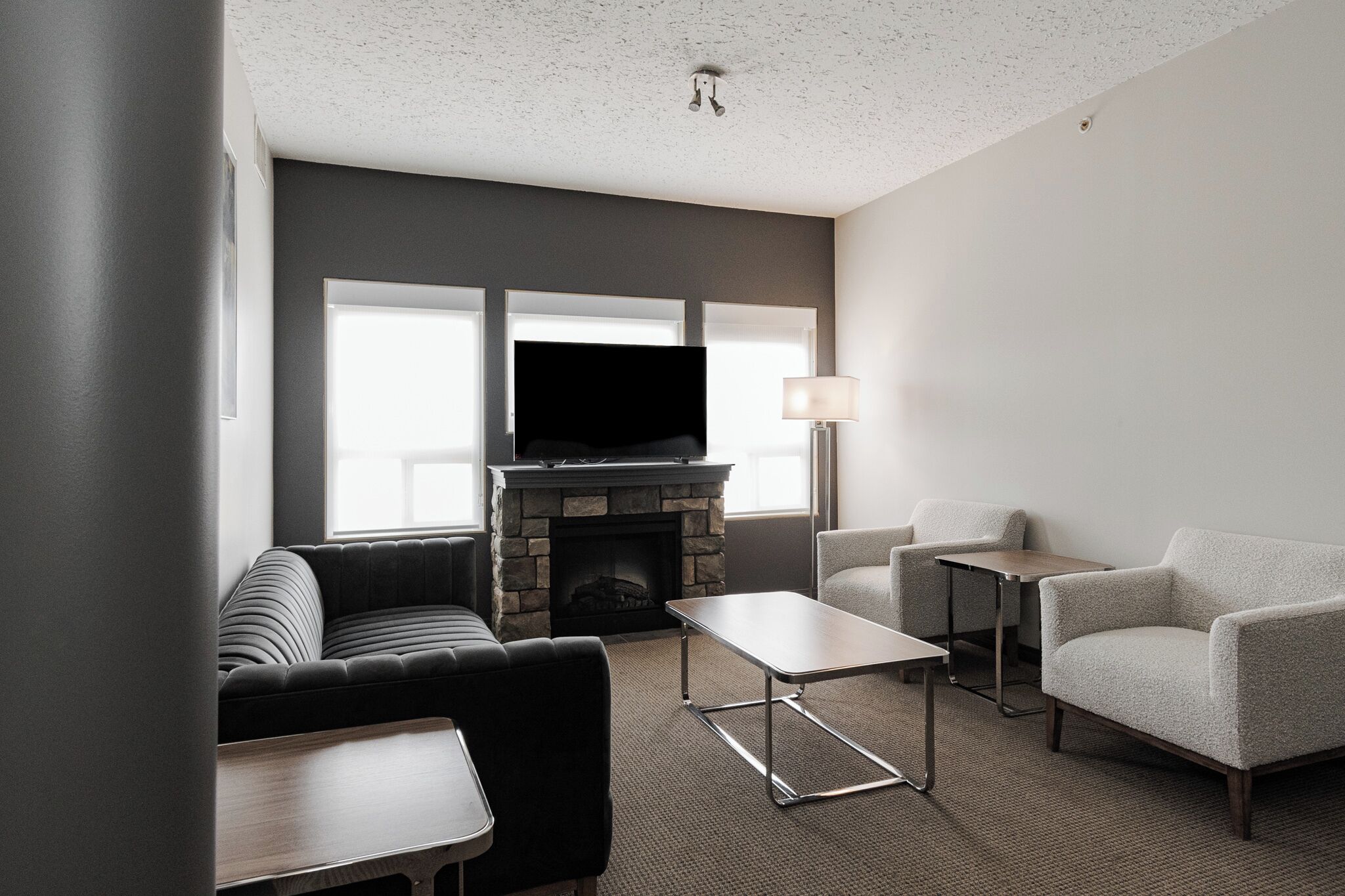 A modern living room with a stone fireplace, a flat-screen TV, a sofa, two armchairs, and a small table.
