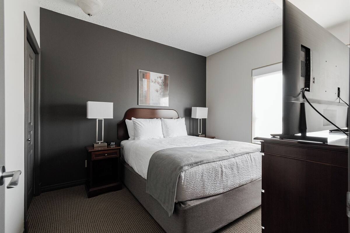 A hotel room with a bed, bedside tables, a TV, and a window.
