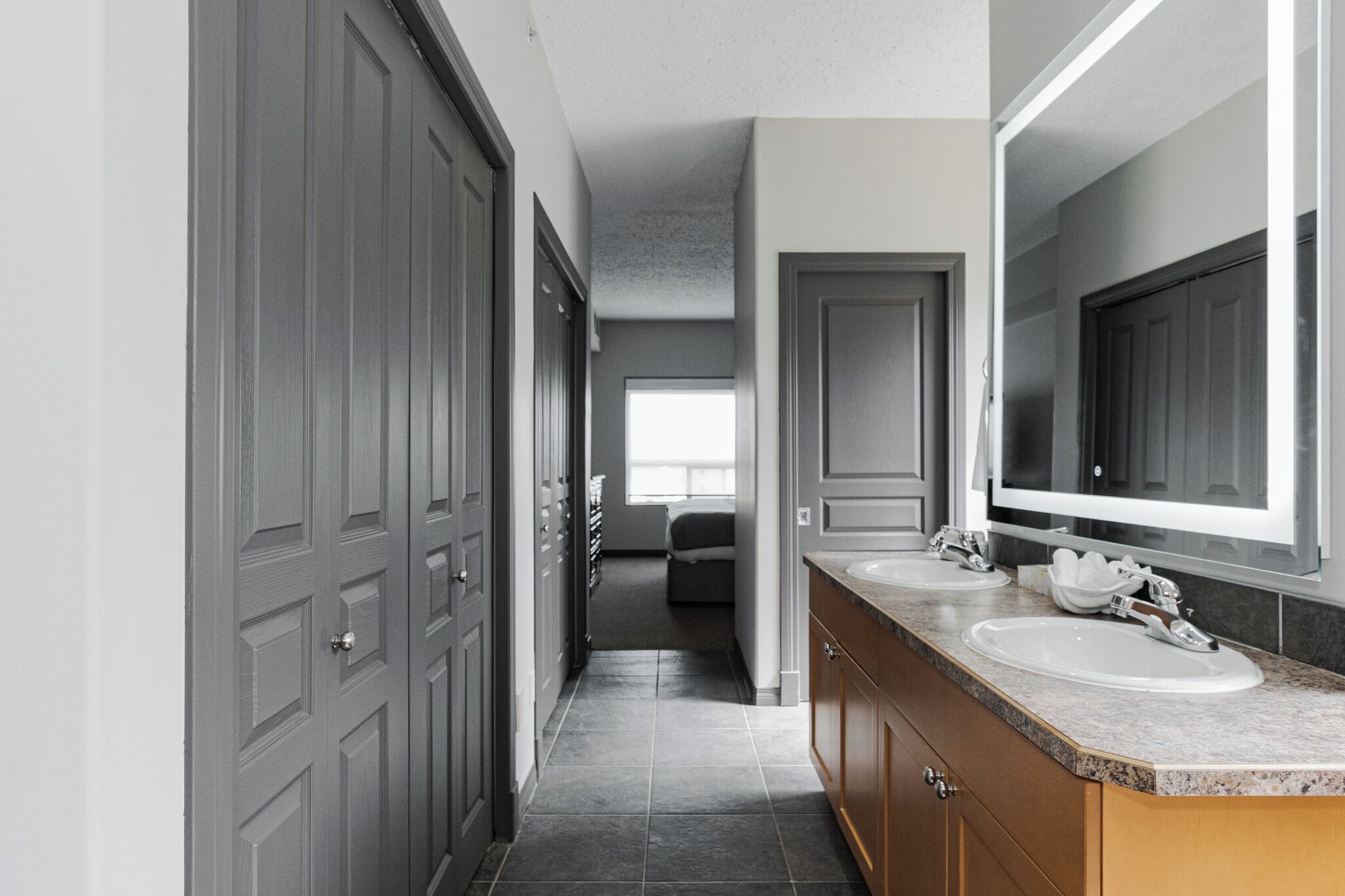 A modern bathroom with a large mirror, two sinks, and a walk-in closet.
