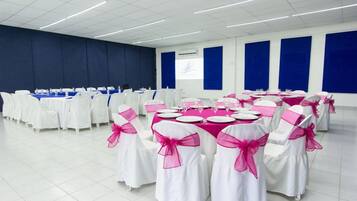 A conference room with tables set for a meeting, white chairs with pink sashes, and blue acoustic panels on the walls.