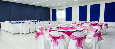 Ein Konferenzraum mit Tischen für eine Besprechung, weiße Stühle mit rosa Bändern und blaue Wandpaneele.