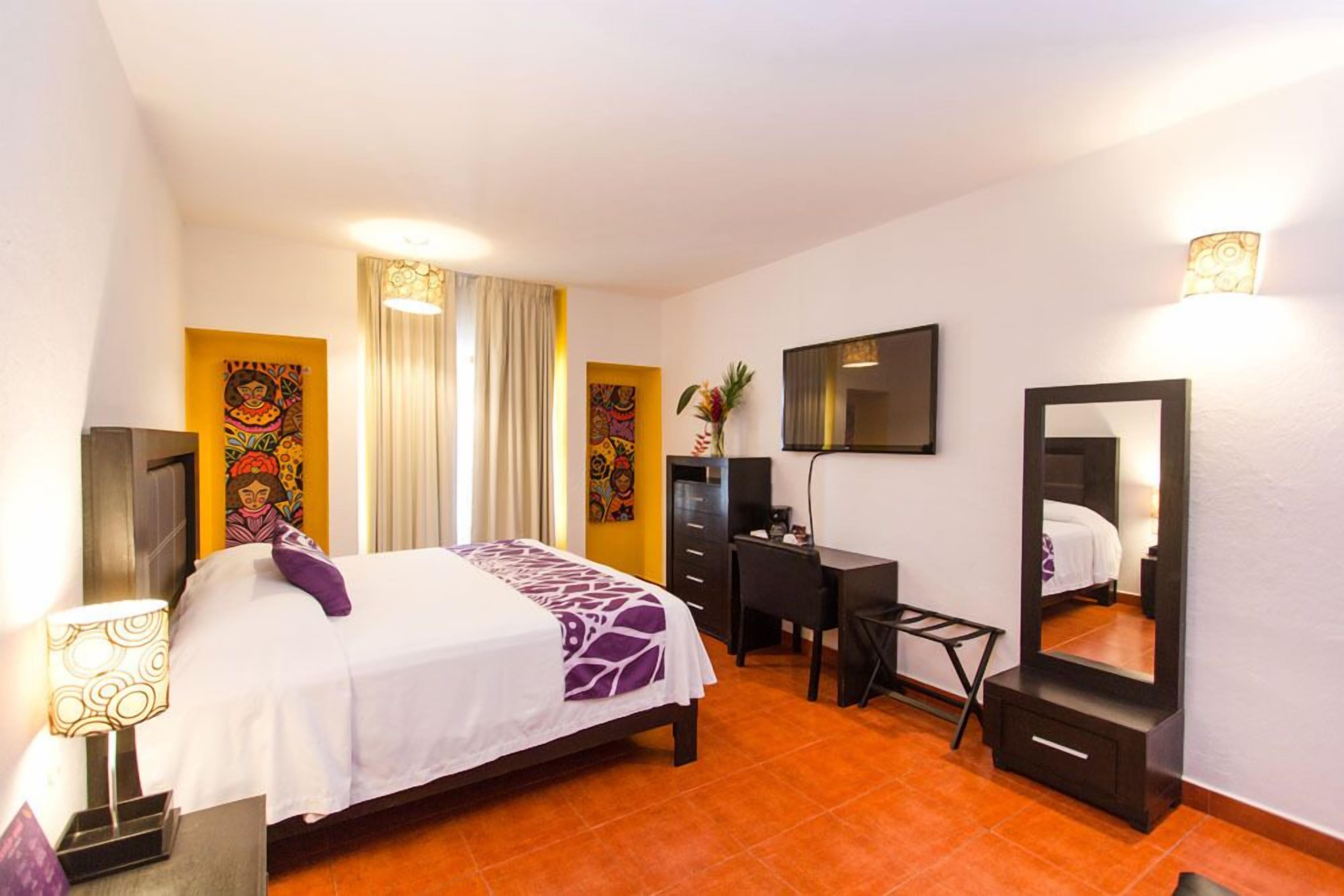 Une chambre d’hôtel avec un lit, un bureau, une chaise et un grand miroir.