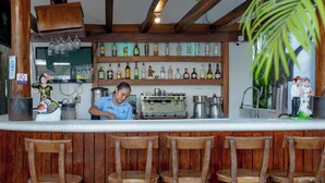 Een barruimte met houten stoelen, een barman en flessen drank op planken.