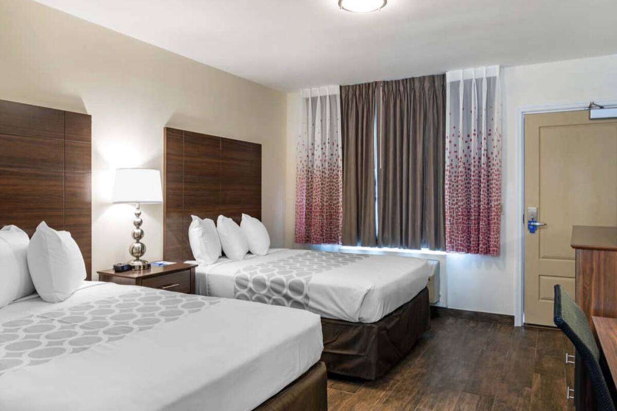 A hotel room with two beds, a desk, a TV, and a door.