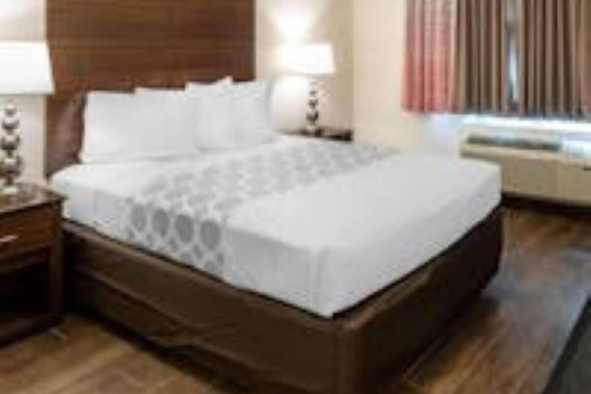 A hotel room with a large bed, wooden headboard, bedside tables with lamps, and a window with curtains.