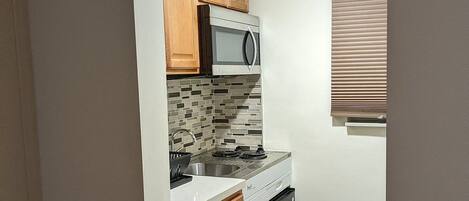 A compact kitchen with wooden cabinets, a microwave, a dishwasher, and a window with blinds.