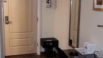 Quarto de hotel com chão de madeira, uma escrivaninha com cadeira, um espelho e uma porta.