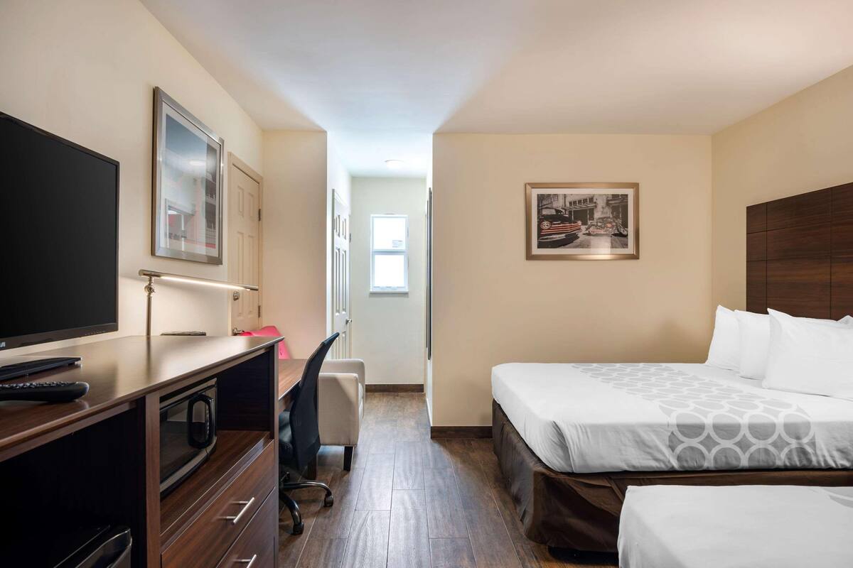 A hotel room with a bed, a desk, a TV, and a framed picture on the wall.