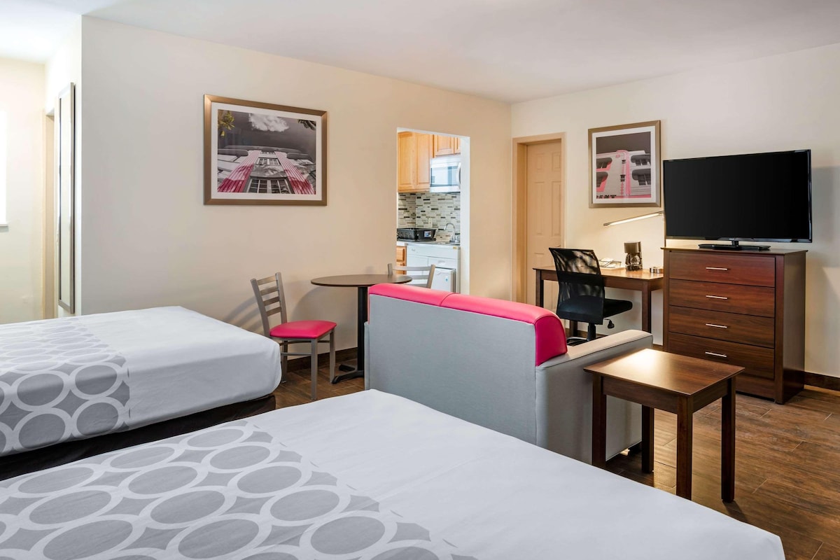 A hotel room with two beds, a desk, a chair, a television, and a small table.