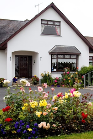 A white building with a brown roof and a small porch. There are colorful flowers in front of the building. - Mourneview B&B (Carlingford)