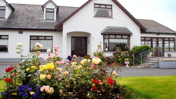 A white building with a brown roof, a dark brown door, and a small window above the door. There is a staircase leading to a porch with potted plants. - Mourneview B&B (Carlingford)