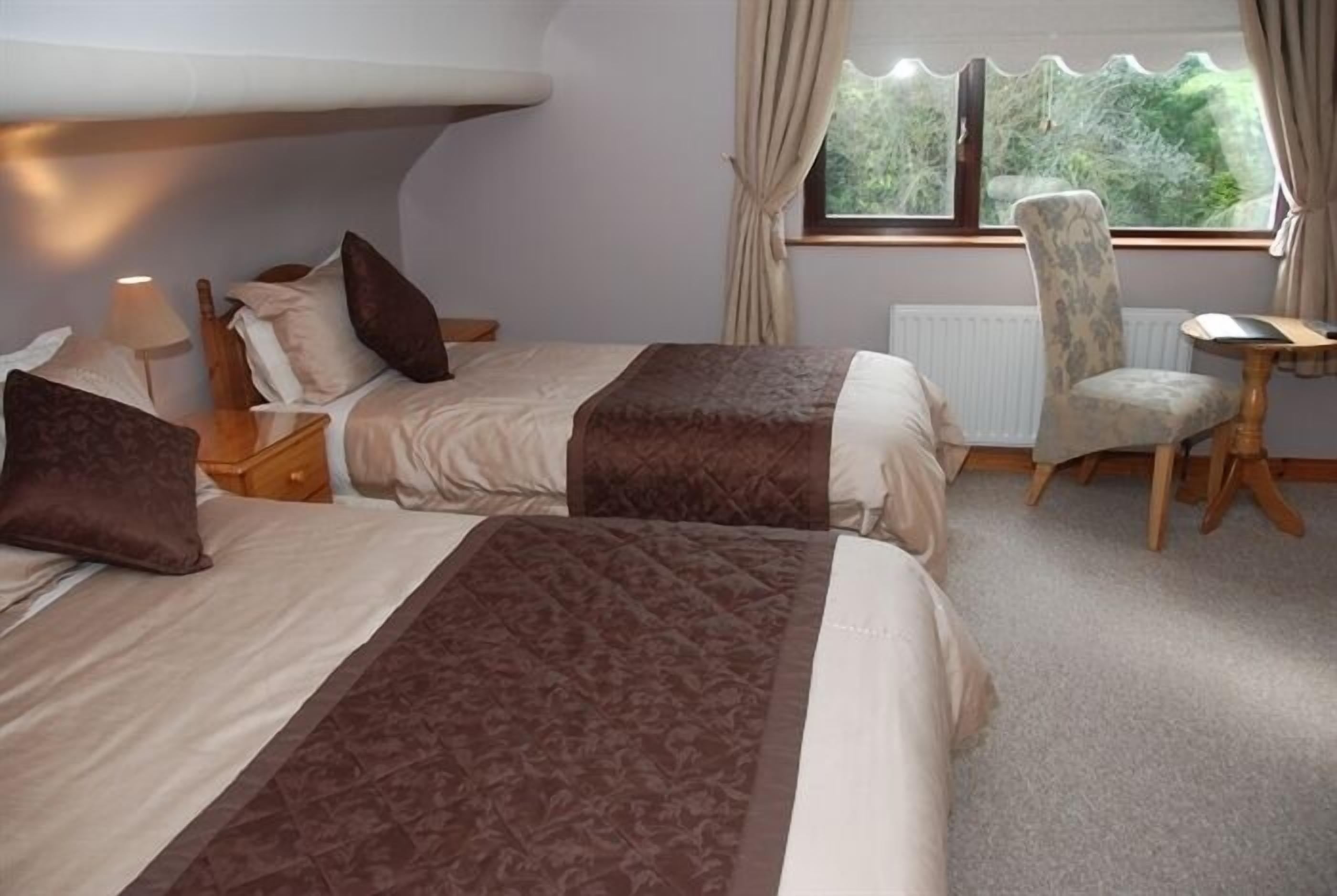 A double bed with a headboard, two bedside tables, a chair, a small table, and a window with curtains.