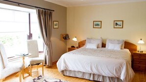 A hotel room with a large bed, two bedside tables with lamps, a chair, a small table, and a window with curtains. - Mourneview B&B (Carlingford)
