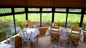 A dining area with tables set for tea service, overlooking a grassy field with sheep. - Mourneview B&B (Carlingford)