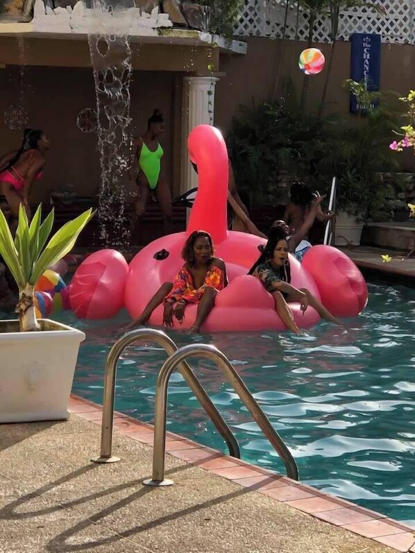 A pool area with a large pink flamingo float, a water feature, and a sign that reads "The Chance." - The Chancellor Hotel (Port of Spain)