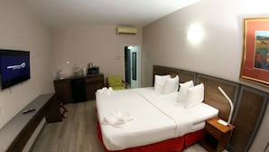Habitación de hotel con una cama, un escritorio con ordenador, un televisor y un cuadro en la pared.
