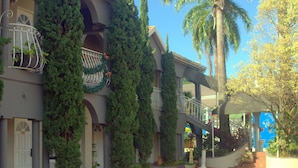 Un edificio de varios pisos con balcones, un paseo techado y diversas plantas en macetas.