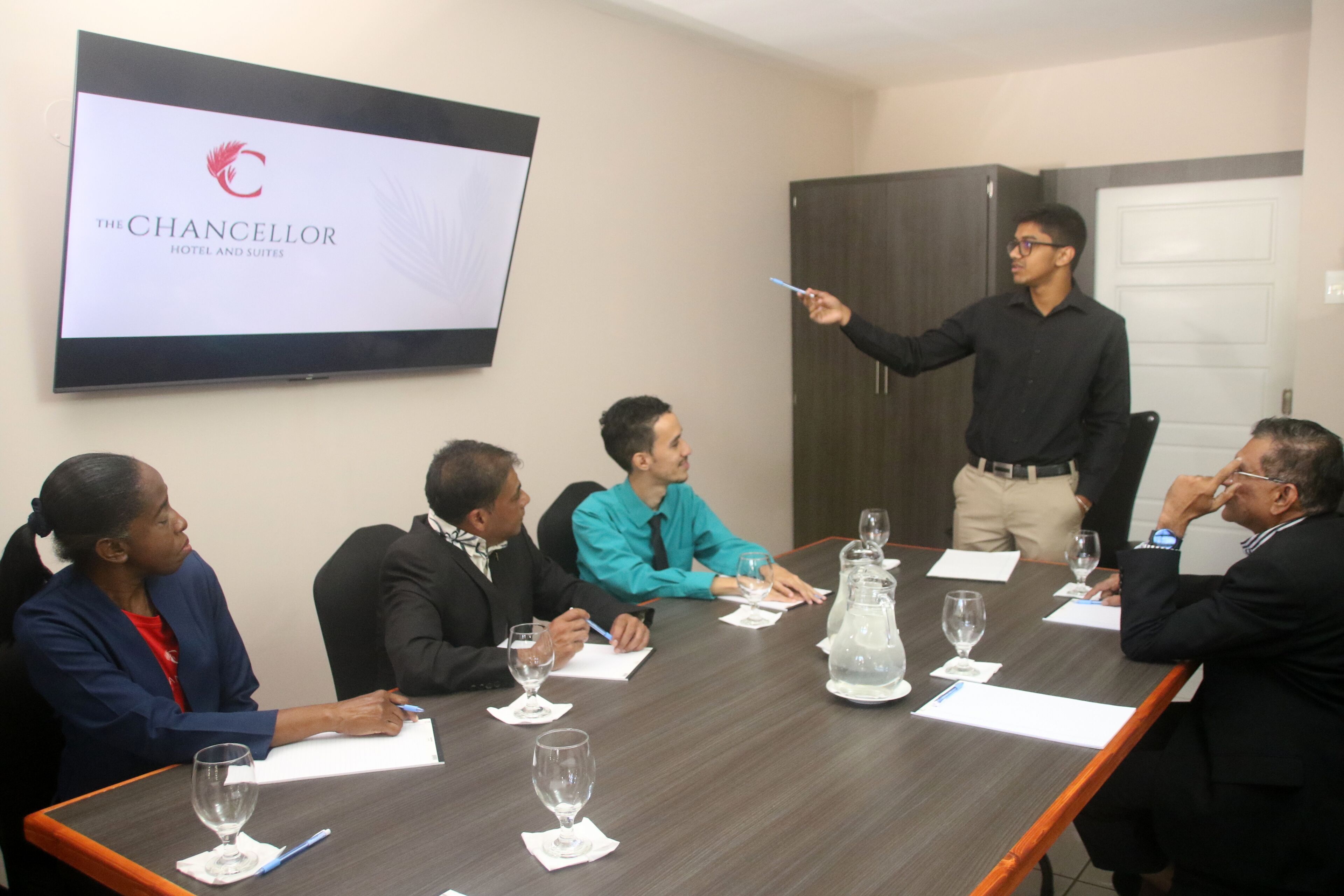 A conference room with a long table, several chairs, and a screen displaying a logo.