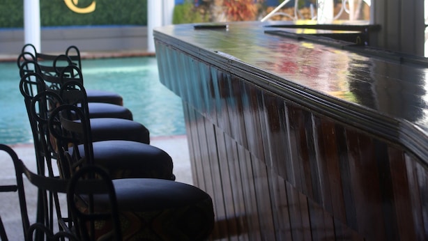 Zona de bar con vista a la piscina, taburetes y una pared decorativa con un logotipo.