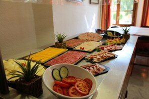 Une table de buffet proposant divers aliments, notamment des tomates et des concombres en tranches, ainsi que différents types de viandes.