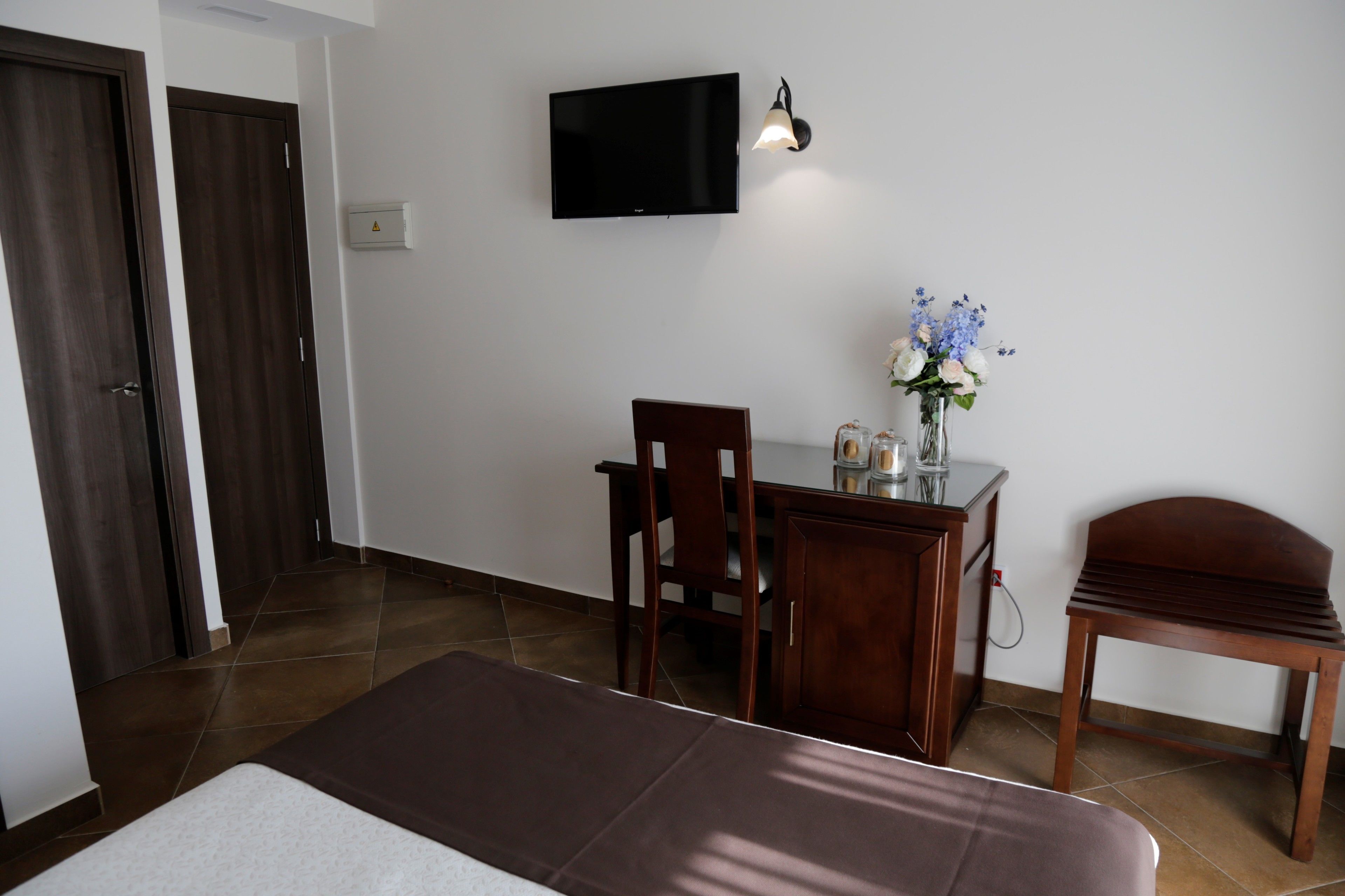 Une chambre d’hôtel comprenant un lit, un bureau avec une chaise, une télévision et un vase avec des fleurs.