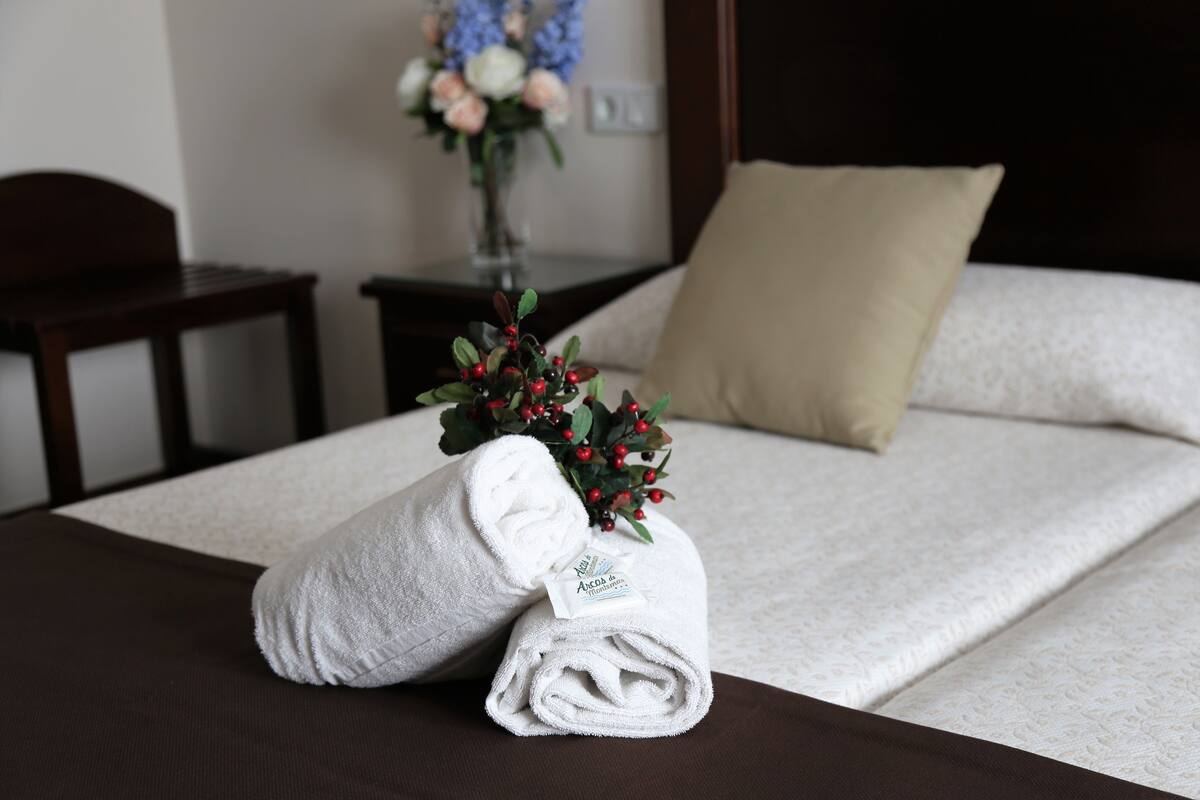 Una cama bien hecha con una toalla blanca y un pequeño ramo de flores.