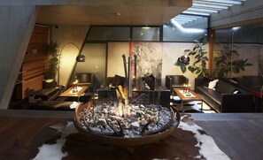 A modern living room with a central fire feature, seating, and a view of the sky through a skylight. - Lux Alpinae (Sankt Anton am Arlberg)